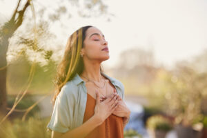 Young woman with hand on chest breathing in fresh air, demonstrating energy management.